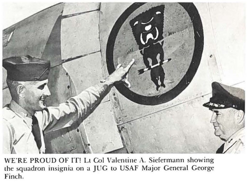 WE'RE PROUD OF IT! Lt Col Valentine A. Siefermann showing the squadron insignia on a JUG to USAF Major General George Finch.