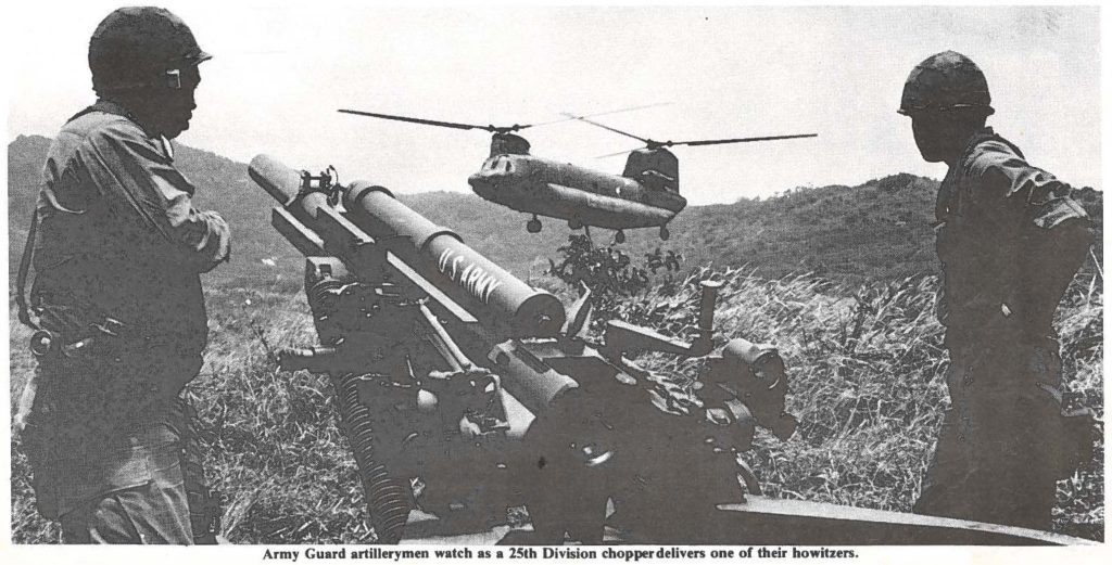 Army Guard artillerymen watch as a 15th Division chopper delivers one of their howitzers.