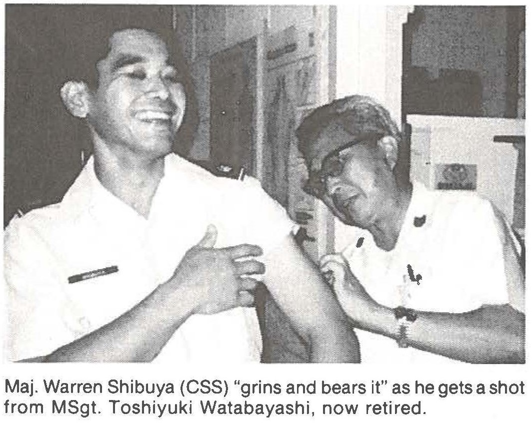 Maj. Warren Shibuya (CSS) "grins and bears it" as he gets a shot from MSgt. Toshiyuki Watabayashi, now retired.