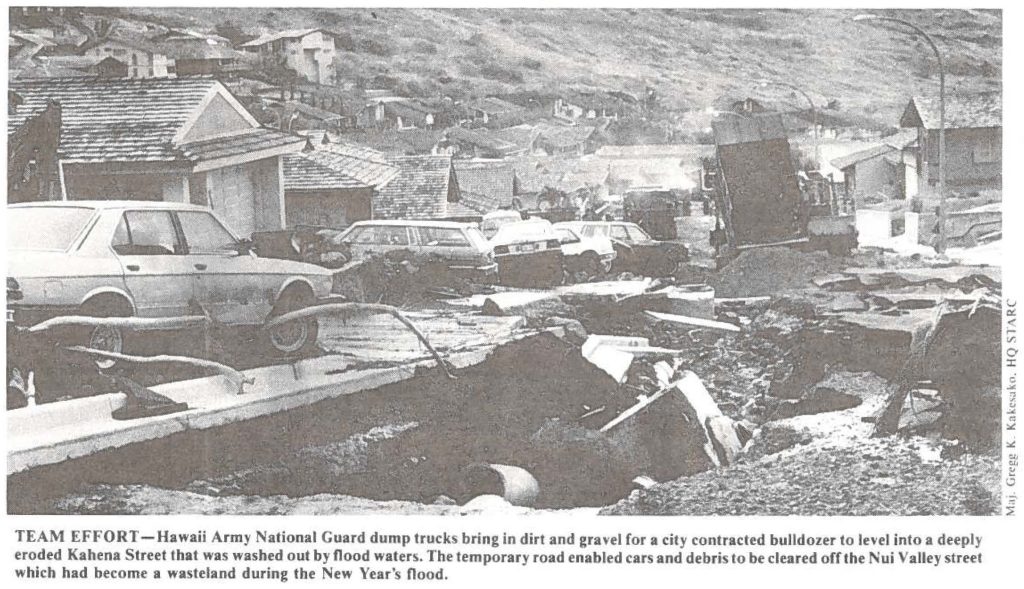 TEAM EFFORT-Hawaii Army National Guard dump trucks bring in dirt and gravel for a city contracted bulldozer to level into a deeply eroded Kahena Street that was washed out by flood waters. The temporary road enabled cars and debris to be cleared off the Nui Valley street which had become a wasteland during the New Year's flood.