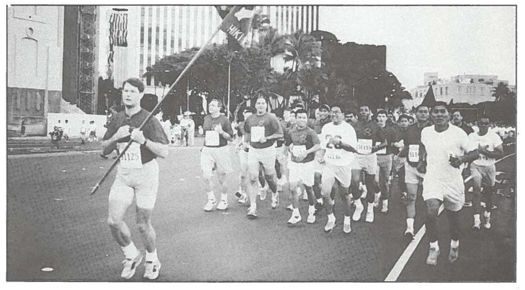 Members of the 1st, Battalion, 487th Field Artillery, with Sgt. Kenneth Barris taking his turn carrying the unit colors, take part in the Great Aloha Run "Sounds of Freedom" military formation.
