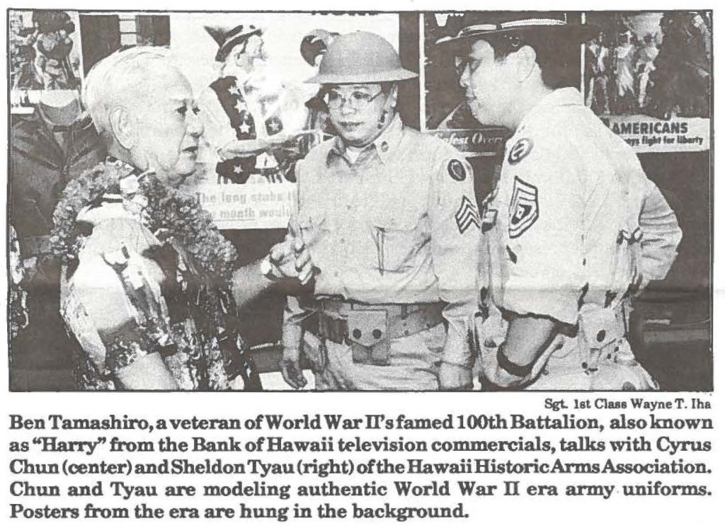 Ben Tamashiro, a veteran of World War II's famed 100th Battalion, also known as "Harry" from the Bank of Hawaii television commercials, talks with Cyrus Chun (center) and Sheldon Tyau (right) of the Hawaii Historic Arms Association. Chun and Tyau are modeling authentic World War II era army uniforms. Posters from the era are bung in the background.