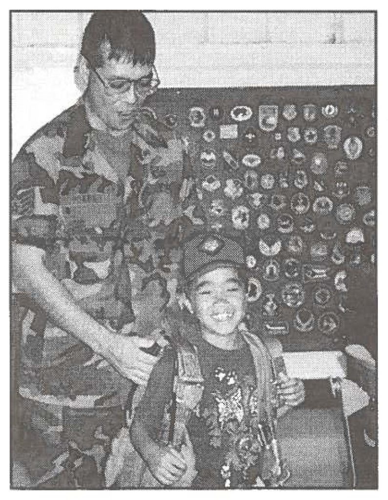 Tech. Sgt. Robert Yokono, from the 154th Wing's Survival Equipment Branch, fits a parachute on Cub Scout Mark Atta. (HlANG photo)