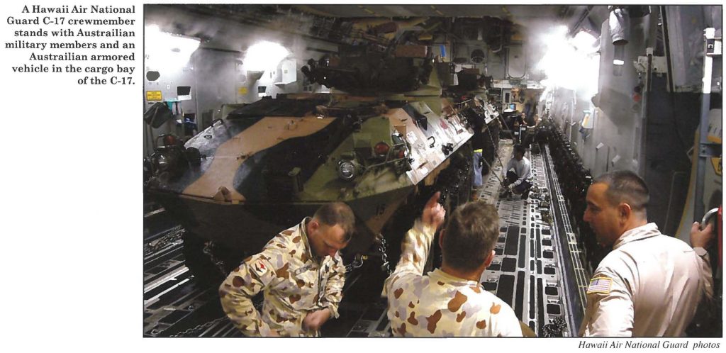 A Hawaii Air National Guard C-17 crewmember stands with Australian military members and an Australian armored vehicle in the cargo bay of the C-17.