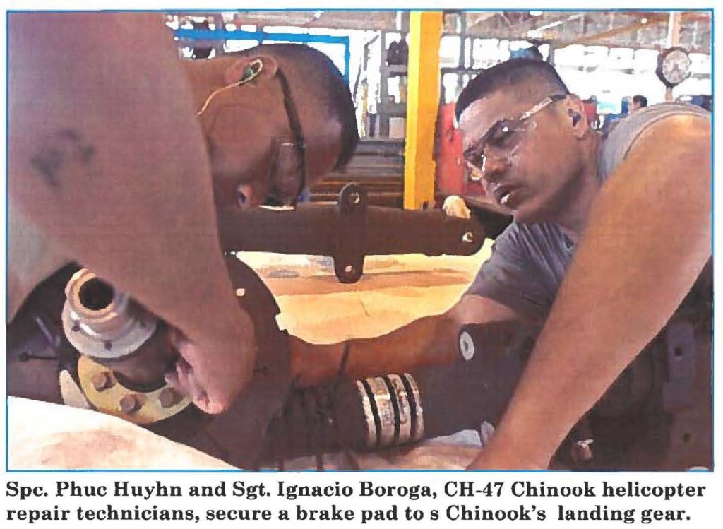 Spc. Phuc Huyhn and Sgt. Ignacio Boroga, CH-47 Chinook helicopter repair technicians, secure a brake pad to s Chinook's landing gear.