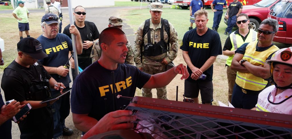 A Kauai County Fire Fighter conducts a briefing on Hazmat conditions to a gathering of first responders during Kauai County Exercise 2017, Pacific Missile Range Facility, Kauai, Aug. 30, 2017. KCE17 was a Hazmat threat and response exercise that brought together federal, state, and county agencies to respond to simulated CBRNE incidents. (U.S. Air National Guard photo by Tech. Sgt. Andrew Jackson)