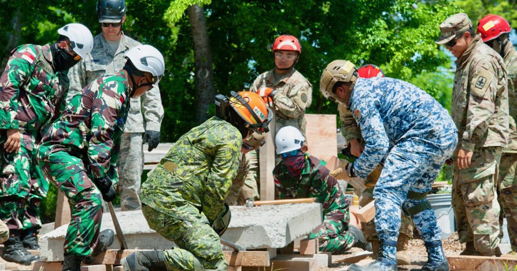 Service members from multiple nations lift up a large cement block during breaching and shoring training as part of the combined - Multinational Task Force [CTF 501] search and extraction training exercise on July 18, 2019 at Kalaeloa Urban Search and Rescue Training area, Hawaii. (U.S. Air National Guard photo by Master Sgt. Mysti Bicoy)