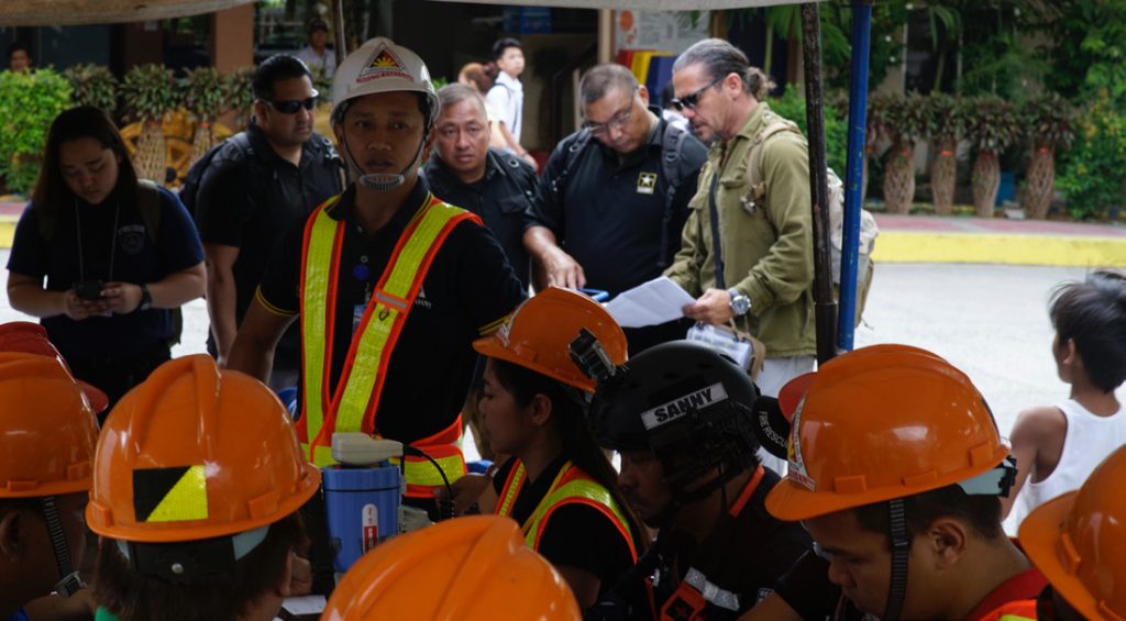 Hawaii National Guard disaster response Soldiers Maj. Wayne Anno, a long with Hawaii
Emergency Management representative David Lopez look on as Batasan Hill Manager, Capt. Jojo
Abad prepares directs his staff in the initial response to an earthquake drill at the beginning of the
field training exercise phase of the Community Disaster Readiness Exercise, Batasan Hills, March
27, 2019. . (U.S. Air National Guard Photo by Tech. Sgt. Andrew Lee Jackson)
