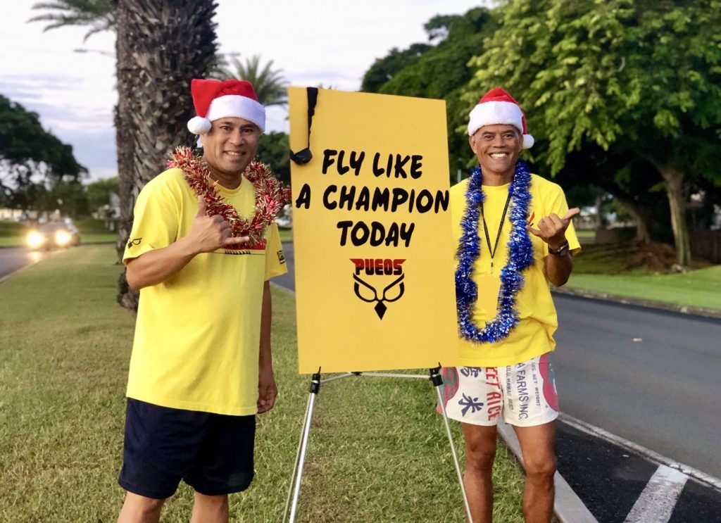 Staff Sgt. Darrell Bactad and Tech. Sgt. Mark Crabbe, 204th Airlift Squadron information managers, welcome inbound traffic as Airmen begin weekend drill Dec. 1, 2018, at Joint Base Pearl Harbor-Hickam, Hawaii. The two friends are advocates of random-acts-of kindness and also longstanding members of the Hawaii Air National Guard Honor Guard team, with nearly 40-years-of-service between the two. (U.S. Air National Guard photo by Senior Airman John Linzmeier)