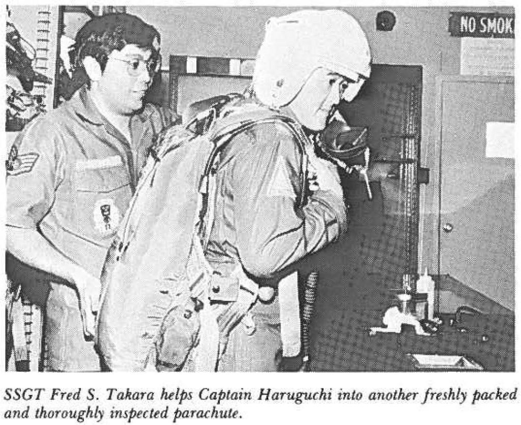 SSGT Fred S. Takara helps Captain Haruguchi into another freshly packed and thoroughly inspected parachute.