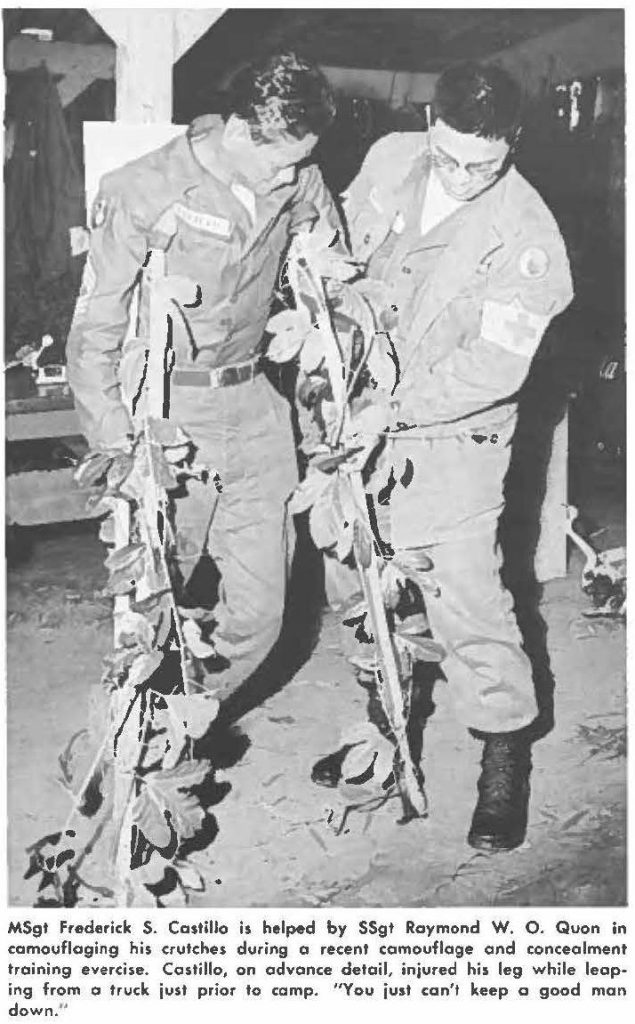 MSgt Frederick S. Castillo is helped by SSgt Raymond W. O. Quon in camouflaging his crutches during a recent camouflage and concealment training exercise. Castillo, on advance detail, injured his leg while leaping from a truck just prior to camp. "You just can't keep a good man down".