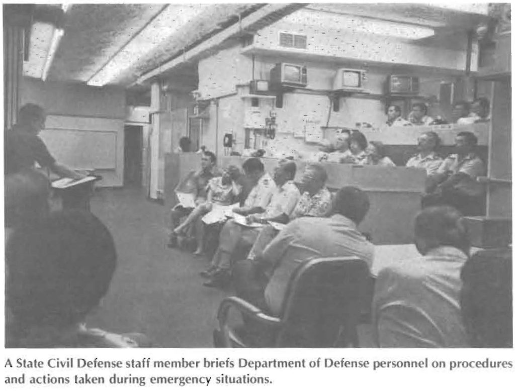 A Slate Civil Defense staff member briefs Department of Defense personnel on procedures and actions taken during emergency situations.