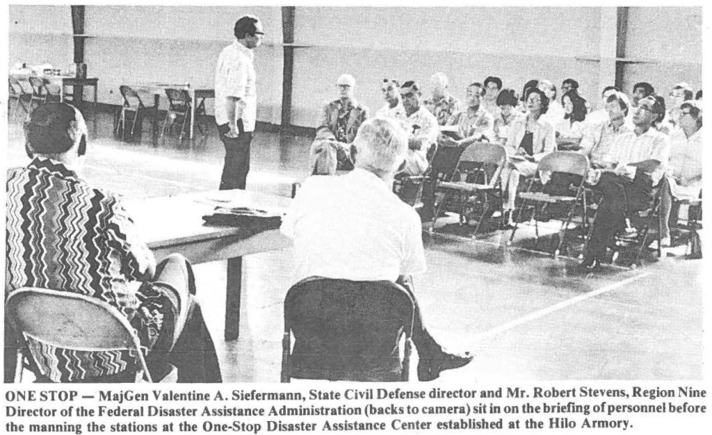 ONE STOP - Maj Gen Valentine A. Siefermann, State Civil Defense director and Mr. Robert Stevens, Region Nine Director of the Federal Disaster Assistance Administration (backs to camera) sit in on the brieC-mg of personnel before the manning the stations at the One-Stop Disaster Assistance Center established at the Hilo Armory.