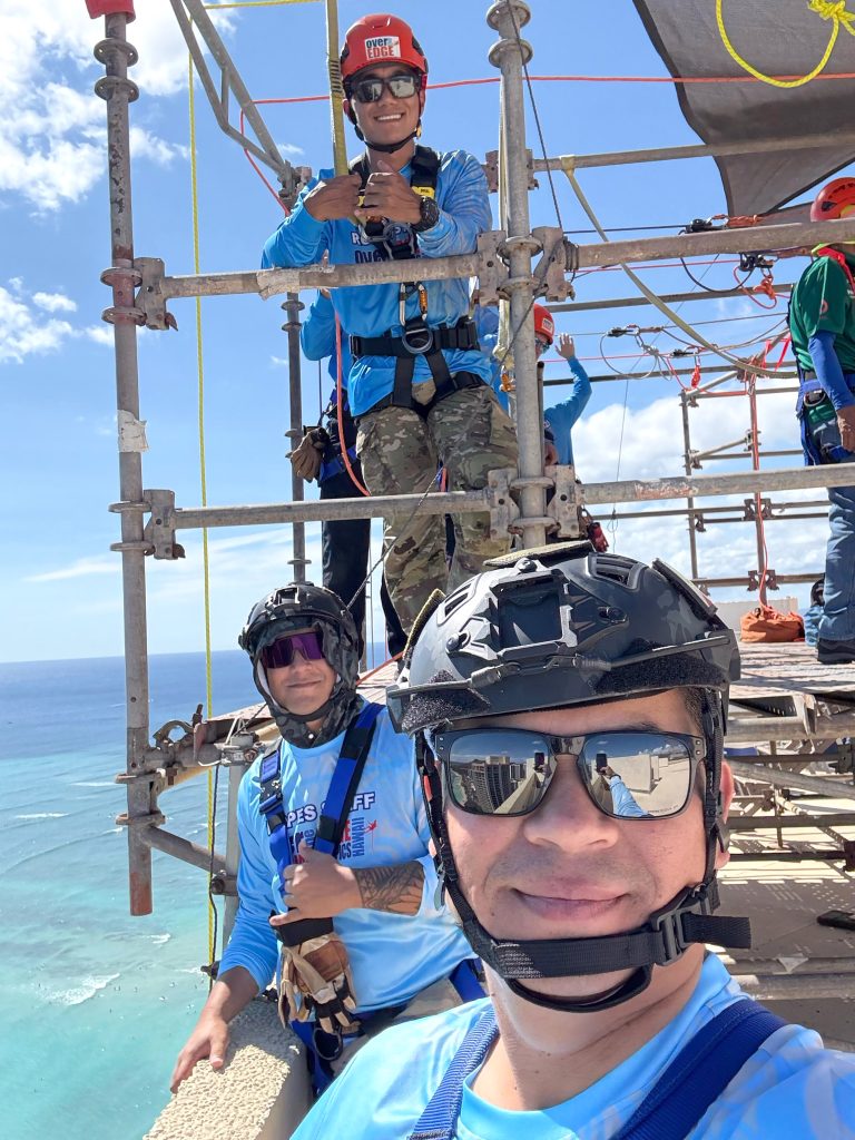 Top right, Sgt. Daysen Chang, Staff Sgt. Jesse Jackola and Specialist Elvis Salinas, atop the 40-story hotel, assisted participants preparing to rappel, ensuring they were securely fastened into their equipment and onto the ropes prior to their descent.