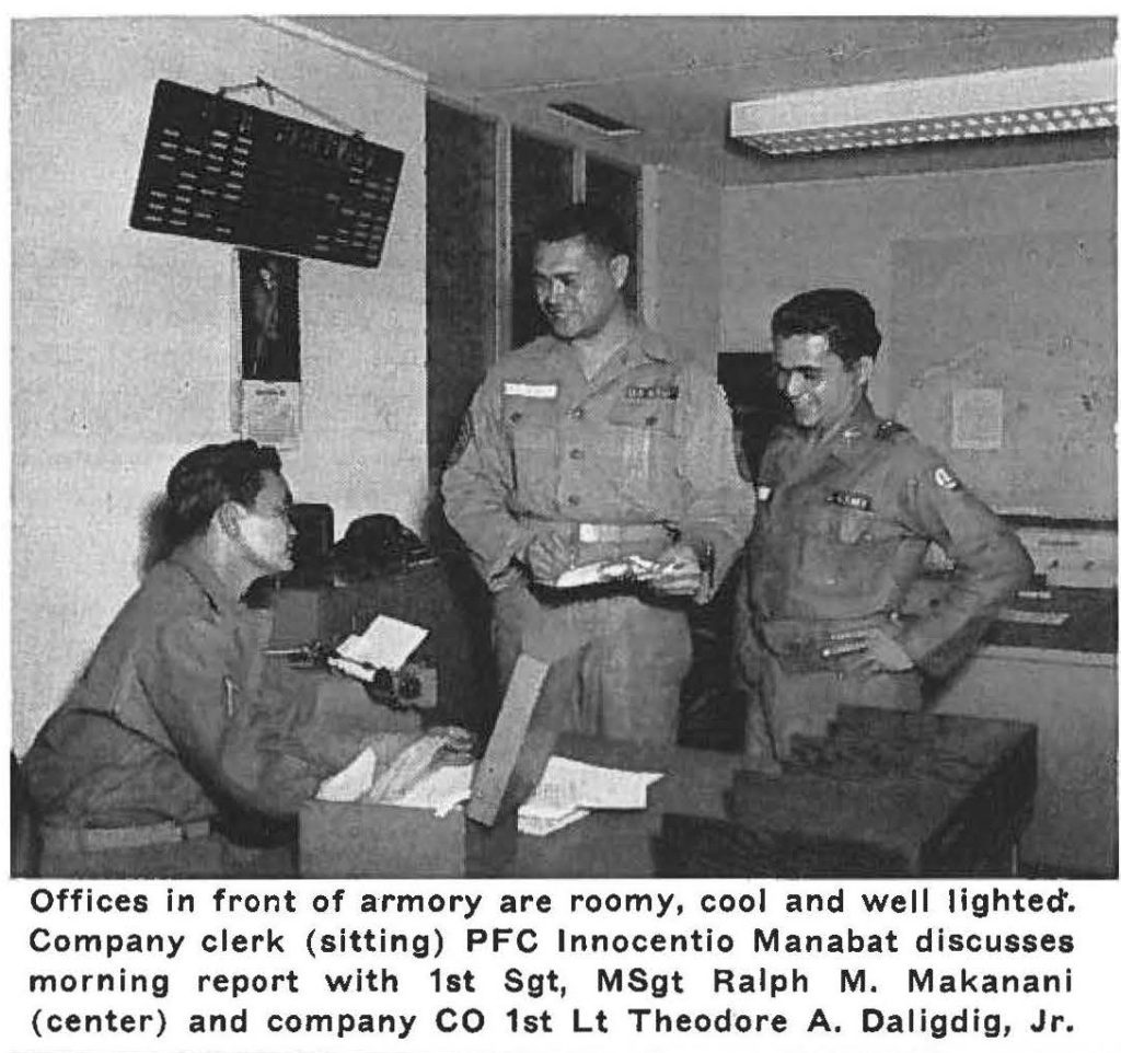 Offices in front of armory are roomy, cool and well lighted'. Company clerk (sitting) PFC lnnocentio Manabat discusses morning report with 1st Sgt, MSgt Ralph M. Makanani (center) and company CO 1st Lt Theodore A. Daligdig, Jr.