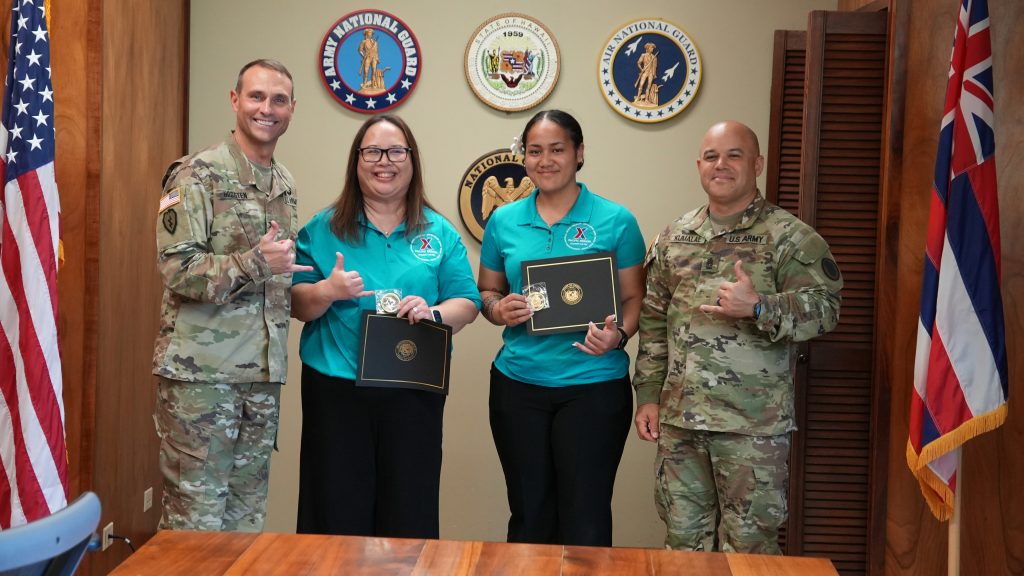 Col. Ronald Hogsten and Command Sgt. Maj. Brandon Kumalae present TAG coins and certificates of appreciation to members of the Schofield Military Clothing and Sales, Mary Ellis and Luluvita Toluvao, for their incredible effort issuing the HING new boots after the Kona low and April severe weather storms.