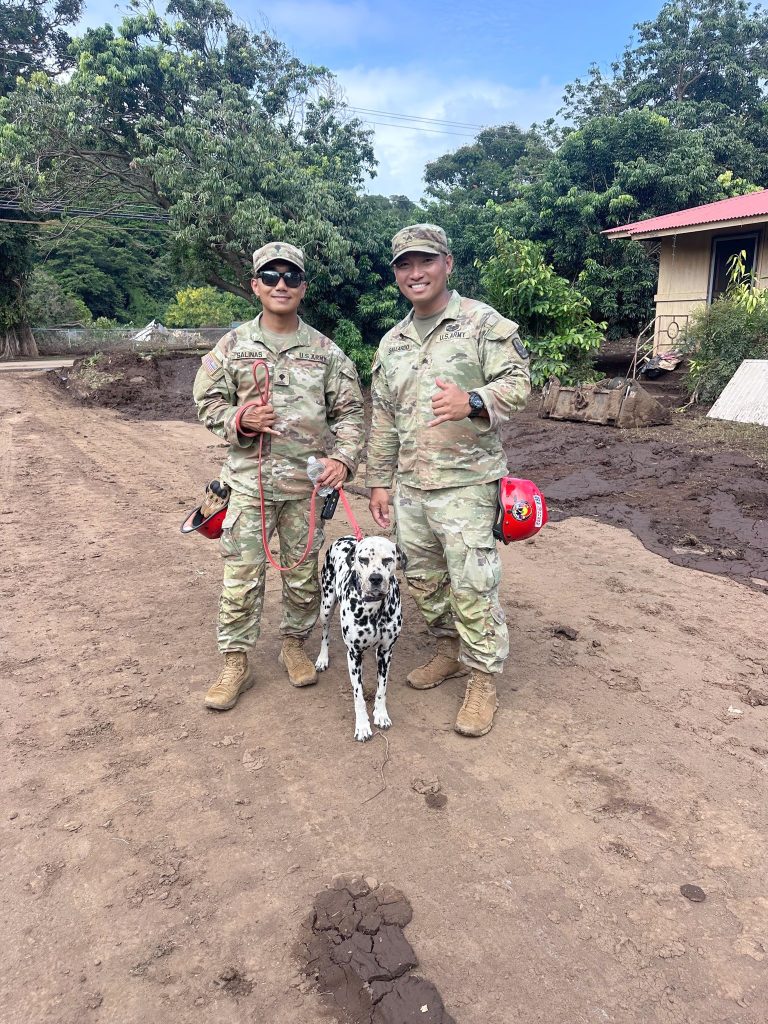 U.S. Army Spc. Elvis Lorenz Salinas, left, and Sgt. Paul Gallardo, both assigned to the 29th Infantry Brigade Combat Team, Hawaiʻi Army National Guard, stood in the driveway of the Galimba home with the family dog, during disaster response operations in Waiʻōhinu, Hawaiʻi, August 2026. (Photo courtesy 1st Lt. Makena Galimba)